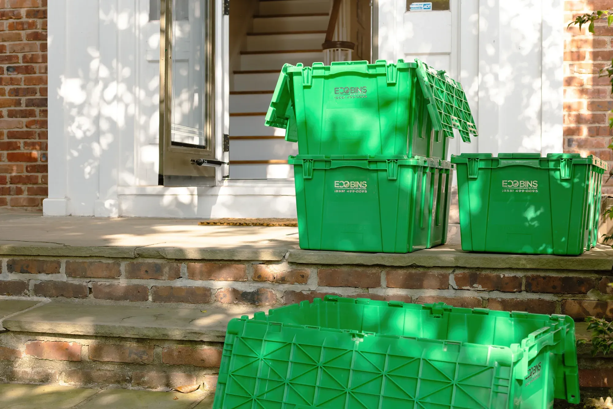 Green EcoBins moving bins stacked on a front porch, delivered ready to pack