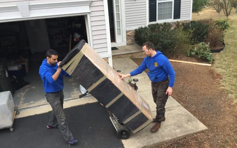 Two Teddy Bear Moving crew members walking a wrapped mattress down a driveway