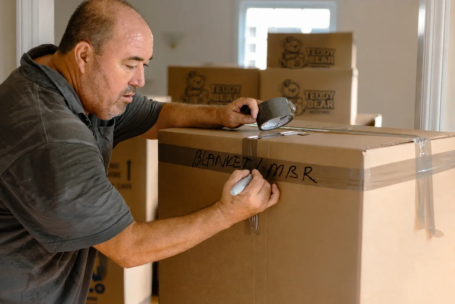 A mover taping and labeling a packed moving box