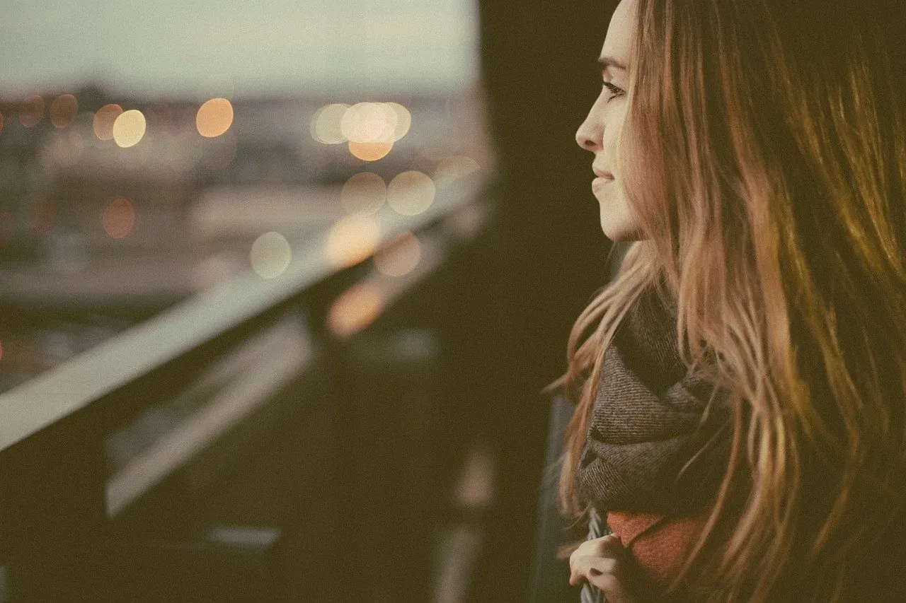 Woman gazing at city lights from balcony